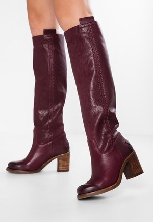 Burgundy leather knee-high boots with a rounded toe, textured finish, and stacked wooden heel, featuring stitching and pull tabs.