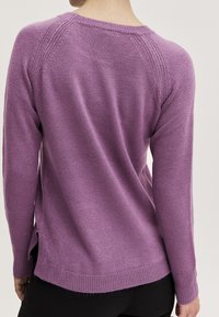 Lila Strickpullover mit langen Ärmeln, geripptem Ausschnitt und Seitenschlitzen am Saum. Glatte Textur und lockere Passform.