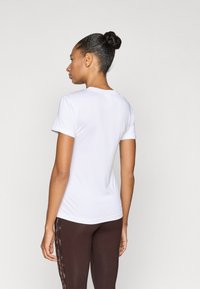 Camiseta blanca de manga corta con cuello redondo, diseño ajustado y textura lisa. Combinada con leggings marrones que presentan un patrón sutil en los laterales.