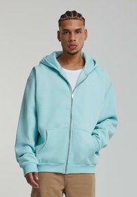 Lyseblå zip-up hoodie med snoretræk i hætten, forlommer og ribbede manchetter. Fremstillet af blødt stof med minimal broderet detalje.