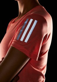 Rode sportieve t-shirt van gestructureerde stof. Met drie reflecterende witte strepen op de linkerschouder. Korte mouwen en ronde halsontwerp.