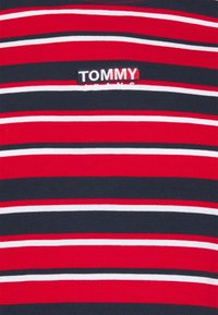 Camiseta de rayas rojas y azul marino hecha de algodón, con un pequeño logo "TOMMY JEANS" bordado en el lado izquierdo.