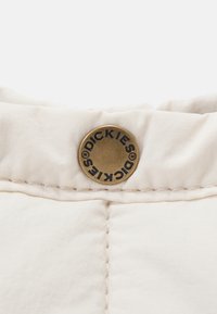 Kremowa tkanina o gładkiej fakturze. Zawiera okrągły brązowy guzik z wytłoczonym napisem "DICKIES". Szew przyszyty wzdłuż krawędzi.