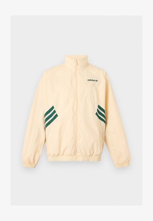 Jasnobeżowa kurtka dresowa Adidas z wysokim kołnierzem, pełnym przednim zamkiem błyskawicznym, elastycznymi mankietami i dołem oraz ciemnozielonym logo i paskami Adidas po bokach.