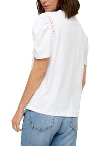 Witte katoenen T-shirt met opgestoken mouwen, voorzien van kantdetails op de schouders. Gecombineerd met blauwe denim jeans, die een relaxte pasvorm laten zien.