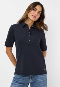 Marineblå polo skjorte med korte ærmer, krave og knaplukning. Har sideslids og et lille logo på kanten.
