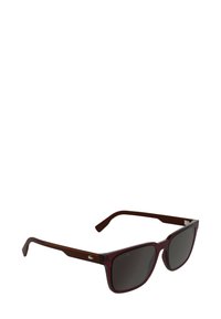 Occhiali da sole quadrati con lenti scure, montatura in plastica color bordeaux e dettagli arancioni a contrasto sulle astine. Logo Lacoste visibile.