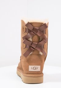 Bruine suède laars met een bontvoering, met een decoratieve achterkant met bruine satijnen linten en een tan rubberen zool. Logo-label aan de zijkant.