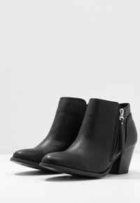 Botas de tobillo negras con exterior de cuero suave, diseño de punta afilada, tacón bajo apilado y cremallera lateral con detalle de borlas.