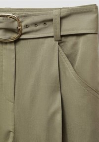 Pantalon vert olive clair taille haute, ceinture en tissu avec boucle ovale dorée, plis devant et coutures inclinées des poches latérales.