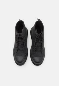 Černé vysoké boty z broušené kůže a gumy. Mají šněrování, strukturovaný svršek a zaoblenou špičku s gumovým krytem.