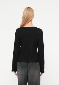 Μαύρο πλεκτό πουλόβερ με υφή, με μακριά μανίκια και ντεκολτέ σκάφος. Συνδυάζεται με γκρι τζιν που παρουσιάζει λεπτομέρειες  στην πίσω τσέπη.