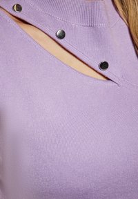 Top rigato viola con un taglio unico, bottoni a pressione argentati e scollatura alta, che enfatizza la texture e il design moderno.