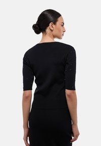 Haut noir en mailles côtelées avec manches courtes, orné de décorations sur les épaules. Texture lisse, design ajusté.