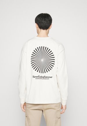Personne portant une chemise blanche à manches longues avec un motif radial noir et le texte « Never Ending Summer MARCOPOLO DENIM » au dos.