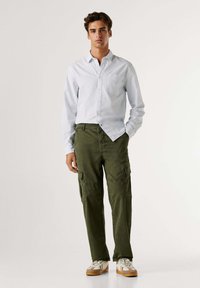 Lichtblauw gestreept overhemdd met knopen en een borstzak, gecombineerd met olijfgroene cargobroek met meerdere zakken en een losse pasvorm.