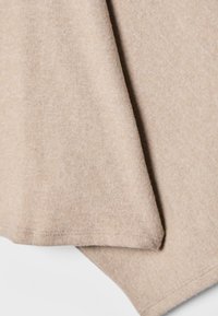 Bež pleteni material, mehka tekstura in gladka površina, z zloženim kotom s čistim robom in minimalnimi barvnimi odstopanji.