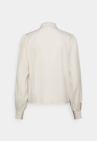 Långärmad blus i krämfärgad med en texturerad yta, volangkrage och knappade manschetter, med en avslappnad passform och lätt gathers vid axlarna.