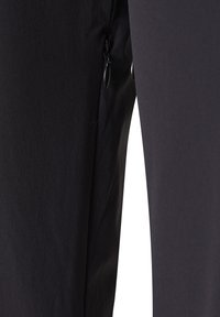 Nærbillede af sorte stofbukser med sidelommer med lynlås og sort metal lynlåstrækker.