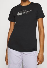 Svart bomullströja med en grå Nike-logotyp över bröstet. Korta ärmar, rund hals och en figursydd silhuett.