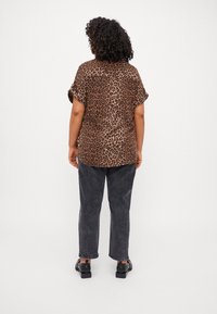 Leopard-print shirt in brown and black fabric, short sleeves, relaxed fit. Worn with dark gray jeans and black shoes.