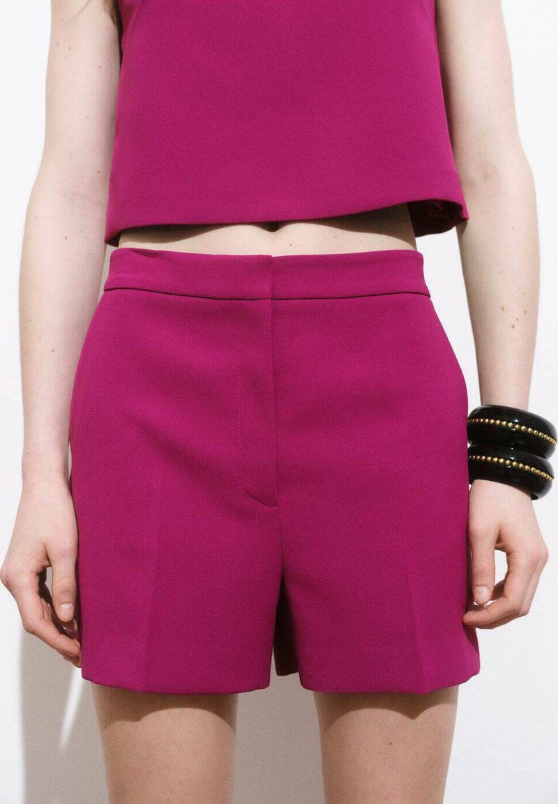Fuchsia shorts med en slät yta, skräddarsydd passform och bred midja; kombineras med svarta armband på handleden.