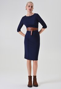 Marineblaues figurbetontes Kleid mit dreiviertellangen Ärmeln, braunem Leder-Gürtelbund und knielangem Schnitt. Glatte Textur mit minimalen Nähten.
