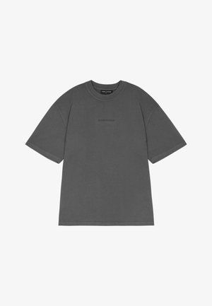 Šedé oversized tričko vyrobené z bavlny, s krátkými rukávy, klasickým kulatým výstřihem a diskrétním logem značky tištěným na přední straně.