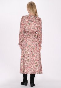 Rochie lungă, cu un model bej și un design paisley roșu și verde, cu mânici lungi, talie elastică și o siluetă fluidă. Botine negre cu toc.
