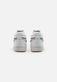 Sneaker bianche con tomaia in pelle liscia, accenti grigi, linguette blu al tallone e suola in gomma leggermente consumata, che mostrano un design minimalista.