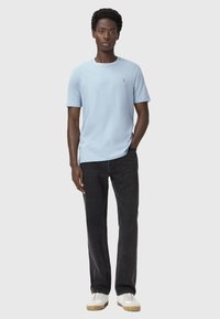 Lyseblå kortærmet t-shirt med rund halsudskæring, parret med sorte denimbukser og hvide sko. Har et diskret logo på brystet.