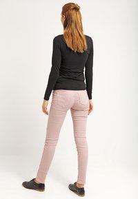 Top nero a maniche lunghe abbinato a jeans aderenti rosa chiaro. L'outfit include scarpe nere e presenta un design con tasche posteriori sui jeans.