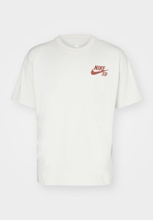 Hvid bomulds t-shirt med rund hals, korte ærmer og et rødt Nike SB-logo på venstre bryst. Enkel, udekoreret design.