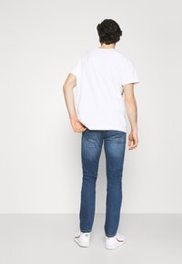 White cotton T-shirt with a crew neck, paired with slim-fit blue denim jeans. The jeans feature subtle stitching details on the back pockets.
