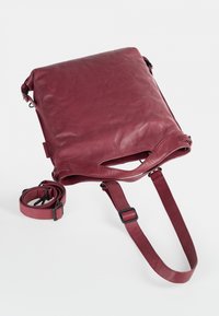 Bordeaux leren draagtas met een gladde textuur, verstelbare schouderbanden en een bovenste ritsclosure. Voorzien van bovenhandvatten en een verwijderbare strap.