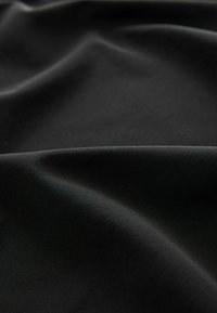 Tessuto morbido e nero drappeggiato in pieghe eleganti, che mette in risalto texture lisce e riflessi di luce sottili. Ideale per abbigliamento o tappezzeria.
