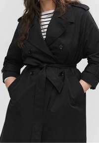 Černý trench coat vyrobený z látky s dvojitým zapínáním, páskem v oblasti pasu a velkými knoflíky. S límcem a bočními kapsami.