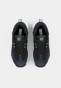 Black athletic shoes with a smooth upper, mesh detailing, white soles, and a logo on the tongue. Features six eyelets for laces.