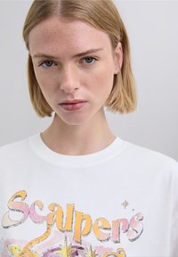 White sweatshirt featuring colorful graphic print with the word "Scalpers" in stylized font, capturing a casual and modern look.
