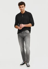 Czarna, długorękawowa koszulka polo, szare dżinsy i czarne sneakersy. Dżinsy mają standardowy krój z delikatnym przetarciem; polo ma kołnierz zapinany na guziki.