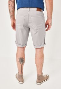 Gray denim shorts with rolled cuffs, back pockets, and a brown leather patch. The wearer has a palm tree tattoo on the calf.