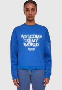 Blauwe sweatshirt met ronde hals, lange mouwen, koord onderaan en witte tekst: "WELKOM IN MIJN WERELD" met het "STRANGER THINGS" logo.