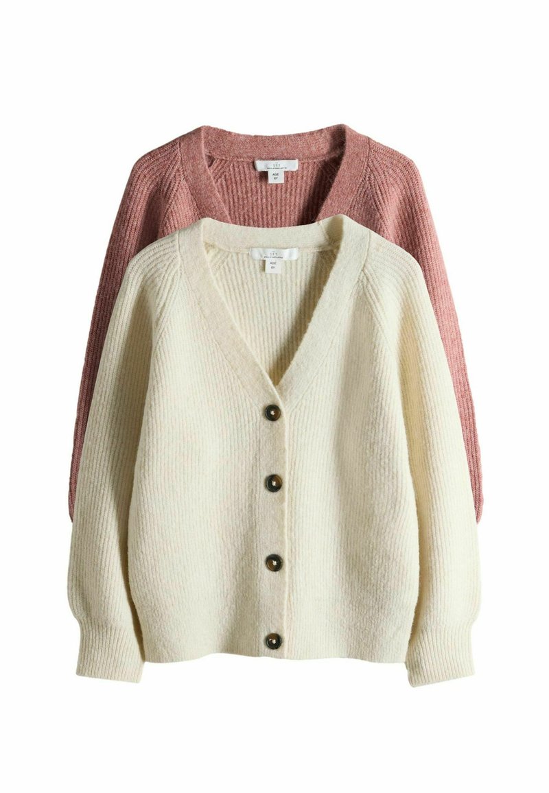 Kaksi neulotun villatakkia: yksi kerma, jossa on V-kaula-aukko, viisi nappia ja ribbineule; yksi vaaleanpunainen, kerma-villatakin takana, joka esittelee samankaltaista muotoilua.