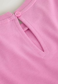 Roza bombažna bluza z okroglim izrezom, ki ima obliko ključavnice na hrbtni strani in majhno ujemajočo se gumbnico. Gladka tekstura po vsej površini.