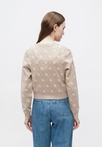 Πλεκτό μπεζ πουλόβερ με διαμαντένο μοτίβο και ανοιχτές αποχρώσεις, ριμπ τελείωμα και φουσκωτά μανίκια, συνδυασμένο με μπλε ψηλόμεσα τζιν.