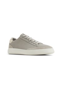 Zapatilla de color gris claro fabricada con un tejido texturizado, con una puntera suave, diseño de cordones y una suela de goma blanca. Presenta un sutil acento beige en el talón.