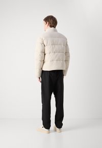 Geacă puffer într-o nuanță bej deschis, cu secțiuni matlasate, guler înalt și croială scurtă. Asortată cu pantaloni negri, cu croială relaxată și adidași.
