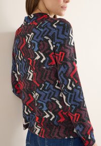 Czarny top z długim rękawem ozdobiony kolorowym wzorem w zygzak w odcieniach czerwieni, niebieskiego i bieli. Miękka w dotyku tkanina, luźny fason i wysoki dekolt.
