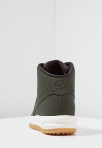 Nike Air sneakers in dark green with a smooth texture, high-top design, white midsole, and gum outsole. Logo visible at the back.