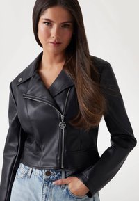 Black faux leather cropped jacket with a double collar, silver zipper, and button detail, paired with light blue high-waisted jeans.